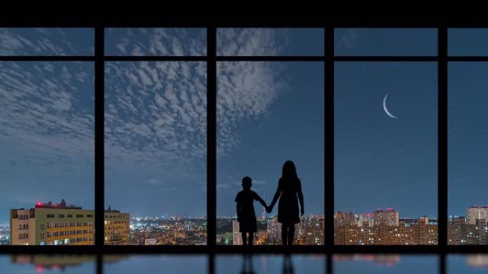 两个孩子站在夜城背景的窗户附近。时间流逝