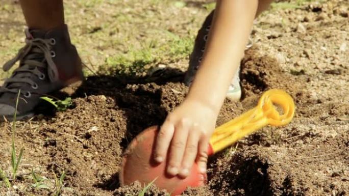 一个小孩子的手在玩塑料铲子挖泥土。特写。