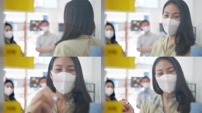 亚洲年轻商人讨论商业集思广益会议，在办公室工作时，他们一起分享数据并用医用口罩书写玻璃墙。