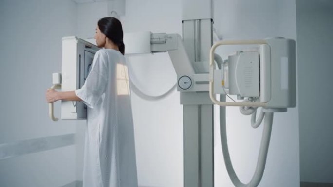 医院放射科室: 穿着医疗礼服的美丽多民族妇女站在x光机旁边，而女医生则对其进行调整。健康患者在护士的