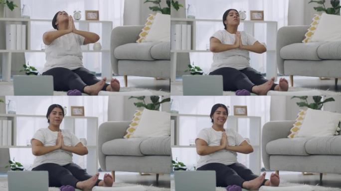 放松的女人在笔记本电脑上数字瑜伽课。健康的黑发女性在现代客厅地板地毯上冥想。年轻微笑的女性在她的休息