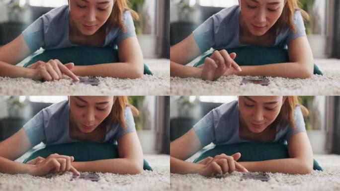 特写年轻快乐的亚洲大学女性，随意躺在地毯地板上，在家客厅使用智能手机滚动产品在线购物。