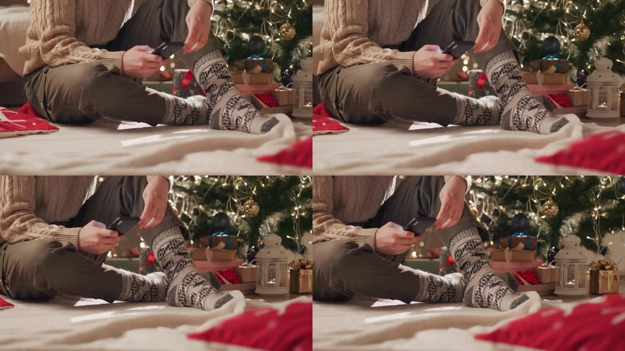 一位穿着圣诞袜的年轻女子坐在圣诞树附近的毯子上，在手机上输入一条消息。