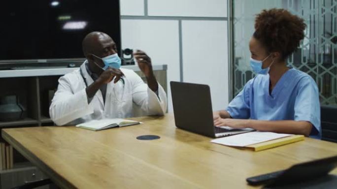戴着口罩的男女医生在办公室使用笔记本电脑讨论