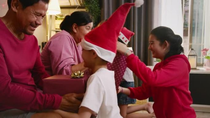 亚洲家庭祖父母在圣诞节期间与家人在家里的客厅庆祝时，向可爱的兄弟姐妹赠送惊喜礼盒。四个兄弟姐妹拥抱和