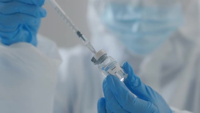 女性在蓝色医用手套中手持新型冠状病毒肺炎疫苗。