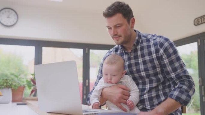 工作的父亲在家中使用笔记本电脑，同时照顾坐在膝盖上的小儿子