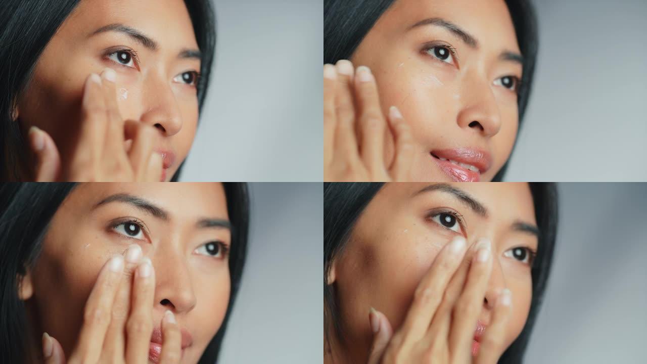 肖像美丽的亚洲妇女轻轻应用面霜面膜感性的姿态在她完美的脸。具有高自尊和健康的年轻成年女性。天然化妆品