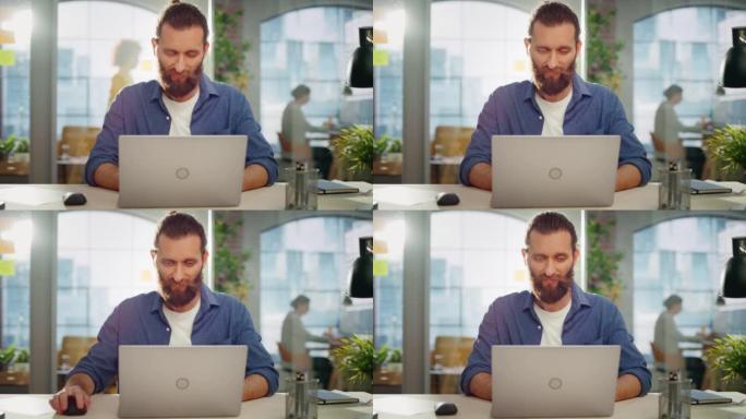 时尚的长发胡子专家坐在创意机构的脸上。年轻的时尚男人在营销公司的笔记本电脑上工作。后台的办公室团队成