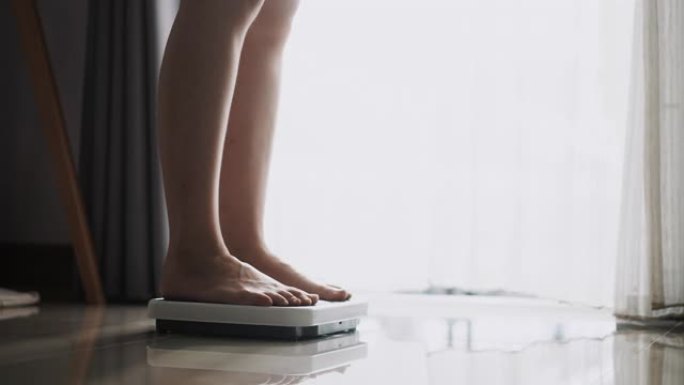 亚洲女性脚踩在数字体重秤上检查她的体重，体重秤