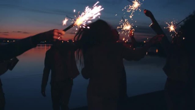 晚上在露天海滩派对上，嬉戏的女孩和男孩在户外用孟加拉灯跳舞的慢动作