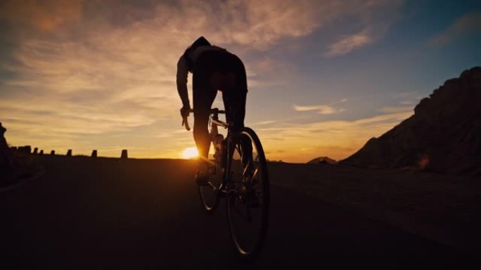 剪影骑车人在日出时在山路上坡骑自行车