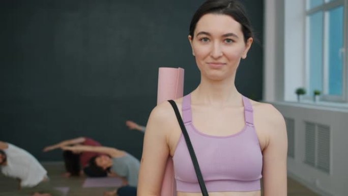 穿着运动服的漂亮年轻黑发女人站在瑜伽工作室微笑的肖像