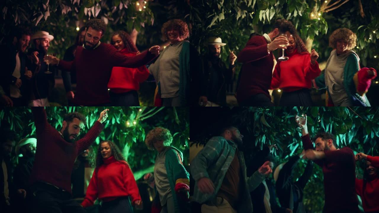 一群快乐的多民族朋友在一个温暖的夜晚举行花园户外派对。男人和女人跳舞，并转向新潮音乐。人们在周末晚上
