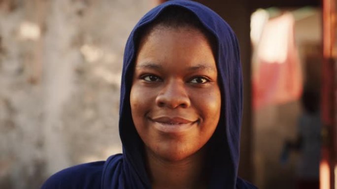 一位穿着传统服装的美丽非洲年轻女子的肖像认真地看着相机，然后微笑着。年轻害羞的女村民代表她的文化