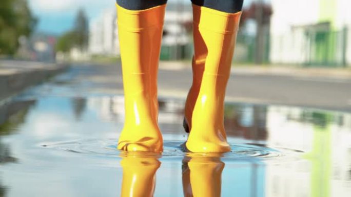 特写: 面目全非的女人穿着黄色雨靴在水坑里跳。