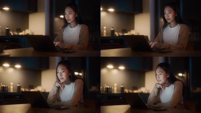 美丽地道的亚洲女人坐在舒适的厨房里的桌子旁，晚上在家使用笔记本电脑。女性在社交媒体上微笑聊天，网上购