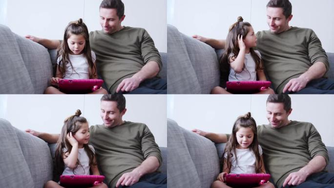 父亲和女儿坐在家里的沙发上一起在粉红色盒子里的数字平板电脑上玩耍