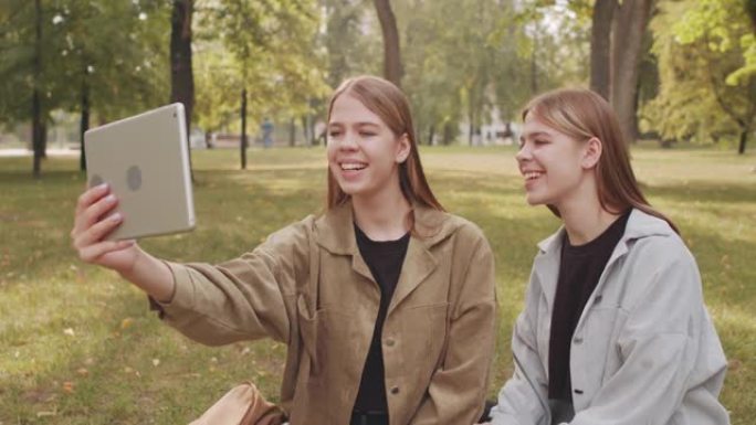 幸福的双胞胎姐妹在公园的视频通话中聊天