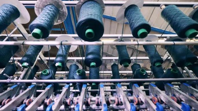 带有螺纹的线轴在工厂机构中缓慢旋转。纺织厂生产设备。