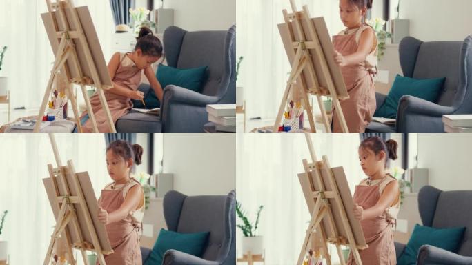 亚洲学步女孩围裙坐沙发椅前绘画帆布把亚克力颜色放在调色板上使用调色板刀混合颜色，在家里的客厅做抽象艺