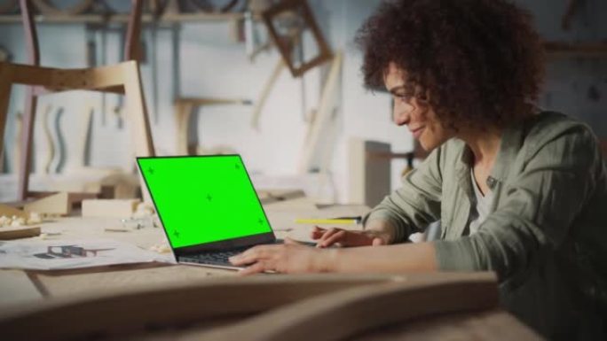 一位多民族家具设计师在带有绿屏模拟显示的笔记本电脑上工作的弧光。创意女性为木工项目准备设计。