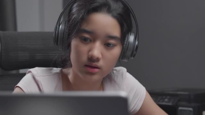 4k分辨率迷人的亚洲少女戴着耳机，在冠状病毒或covid 19锁定时，与老师一起在笔记本电脑上进行在