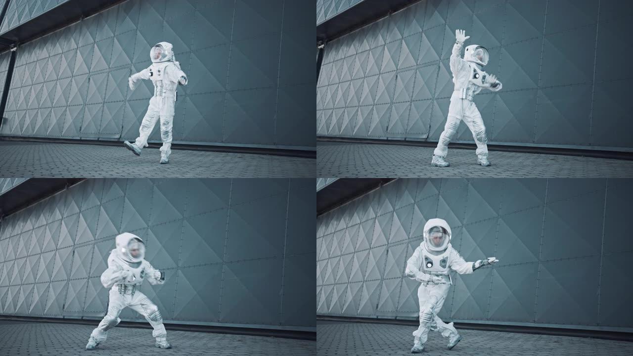 穿着宇航服的英俊男子在金属墙旁边跳舞。宇航员很高兴，并做出了创造性的机器人动作。成功的太空人穿着白色