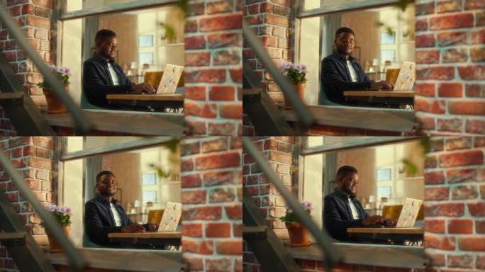 一个年轻的黑人男性坐在办公桌前思考，在笔记本电脑上工作的肖像。创意自由撰稿人在家庭办公室做远程工作。