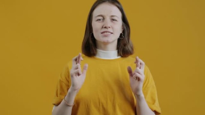 紧张的年轻女士交叉手指并在黄色背景下祈祷的慢动作肖像