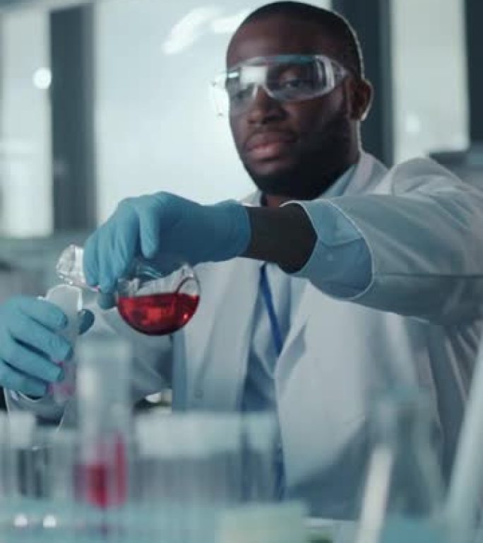 一位非裔美国男性科学家在实验室的试管中混合化学物质的垂直肖像。英俊的黑人微生物学家在现代实验室工作，