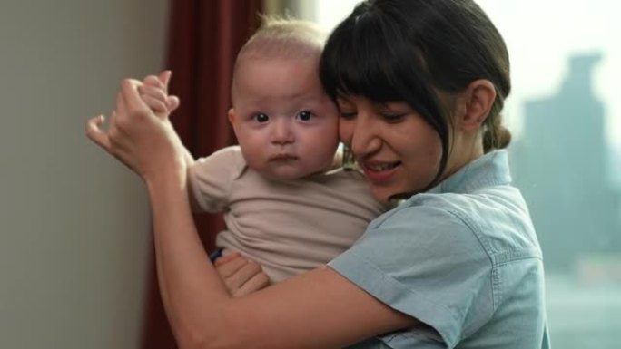 一位美丽的年轻母亲正慈爱地抱着她6个月大的婴儿。她与儿子爱玩，看着相机。