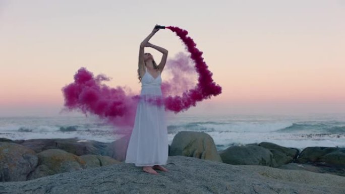 女子手持粉红色烟雾弹清晨在海滩上跳舞庆祝创意自由