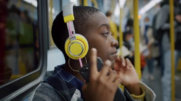 晚上在公共交通工具上戴耳机的年轻黑人妇女的肖像。女非洲裔美国学生从大学回家，听音乐，在繁忙的地铁中放