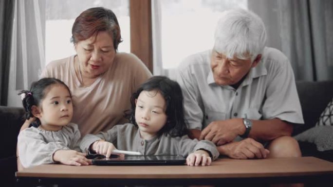 孙儿在数码平板电脑上做家庭作业，与资深成人在家。