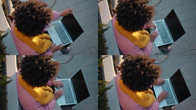 年轻女子坐在城市的长椅上用笔记本电脑工作