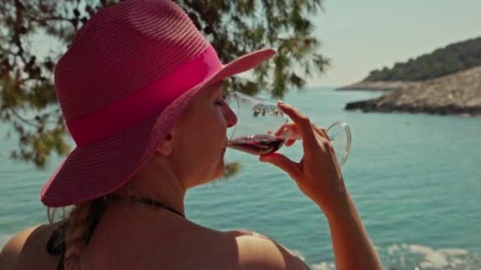 特写金发碧眼的女人，戴着粉红色的帽子坐在海边，喝着一杯酒，赫瓦尔岛