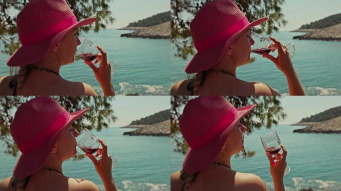 特写金发碧眼的女人，戴着粉红色的帽子坐在海边，喝着一杯酒，赫瓦尔岛