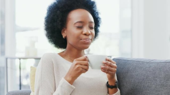 年轻的非洲妇女在家里的沙发上享受一杯咖啡或茶时，感到精神焕发和快乐。非洲裔女性在享受周末的空闲时间时