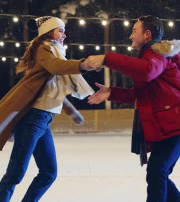 垂直视频。浪漫的冬夜: 滑冰夫妇在溜冰场上玩得开心。美丽的雪落在双人滑冰男孩和恋爱中的女友上，跳舞，