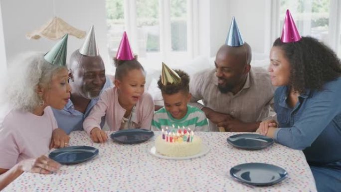 多代家庭坐在家里的桌子旁，用蛋糕和派对庆祝男孩的生日