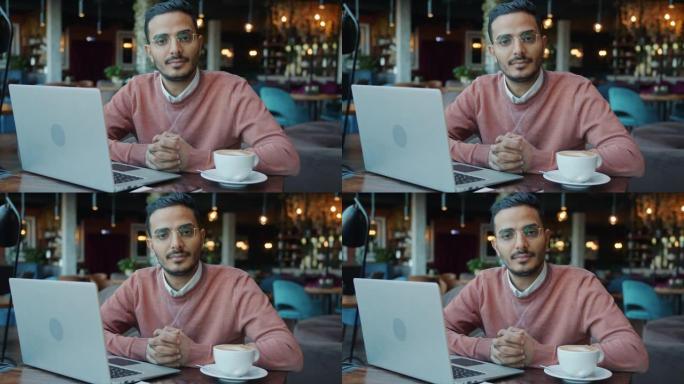 坐在咖啡馆里拿着笔记本电脑和咖啡的迷人阿拉伯商人的慢动作肖像