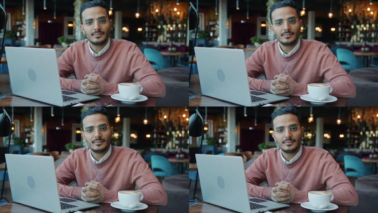 坐在咖啡馆里拿着笔记本电脑和咖啡的迷人阿拉伯商人的慢动作肖像