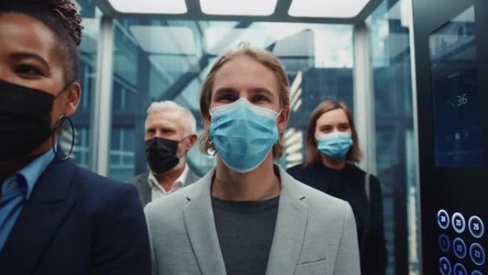 四个戴着防护口罩的多种族国际人士乘坐玻璃电梯在现代商务中心上班。医疗保健、新型冠状病毒肺炎大流行和疫