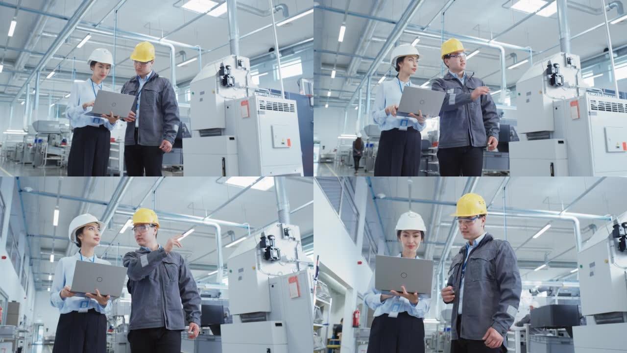 两名年轻的亚洲重工业工程师戴着安全帽，站在笔记本电脑上讨论工厂工作过程的肖像。两名制造业员工在生产设
