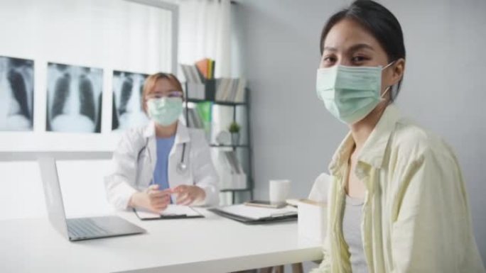 自信的亚洲女医生戴着防护口罩，年轻的病人女孩看着相机，微笑着在诊所或医院的办公桌上进行医疗咨询。