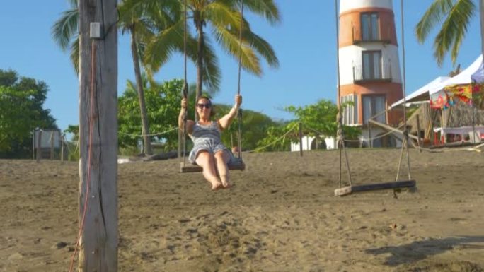 慢动作视频: 微笑的年轻女子在海滩秋千上享受暑假