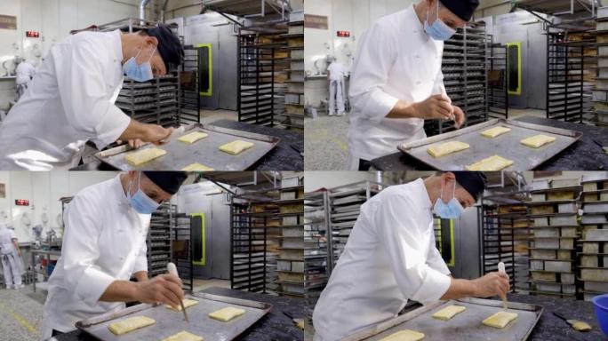 一家工业面包店的主厨用刀装饰糕点面团甜点，然后将其放入烤箱