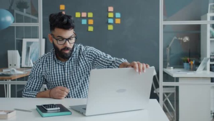不满意的中东员工使用笔记本电脑，然后用拳头敲打桌子并离开工作场所