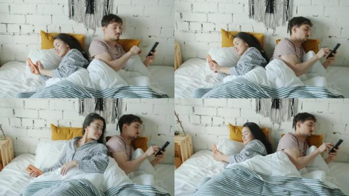 丈夫和妻子使用智能手机在家里的床上互相监视屏幕
